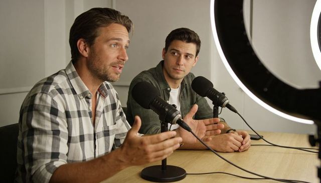 Two podcast cohosts discussing ideas at modern minimalist studio table with ring light