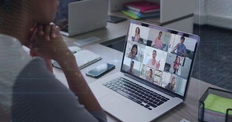 Asian professional watching virtual team meeting on laptop at organized office desk