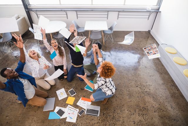 Business team celebrating success by tossing papers in a creative office. Ideal for illustrating teamwork, collaboration, and a positive work environment. Perfect for articles on startup culture, innovative workspaces, and employee satisfaction.