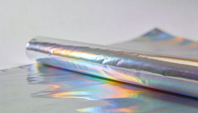 Holographic iridescent foil roll reflecting rainbow light on glossy surface for crafts