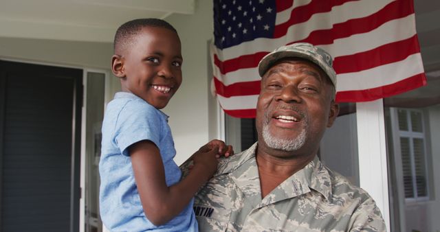 Elderly African American military veteran joyfully holding his smiling grandson in front of an American flag. This heartwarming moment exudes themes of family bonding, patriotism, and generational pride. Ideal for illustrating veteran stories, family values, patriotic concepts, and celebrations of military service.