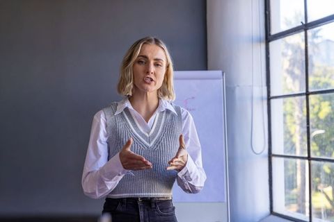 Leading training session gesturing confidently by flip chart near window in modern office