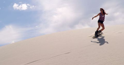 Woman Enjoying Sandboarding on Desert Dunes under Blue Sky