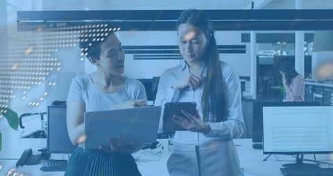 Two colleagues collaborating over tablet and laptop in modern open-plan office workspace