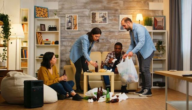 Friends cleaning up after casual living room gathering picking up beer bottles and trash