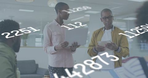 Collaborating team analyzing data on laptop and tablet with floating numbers overlay