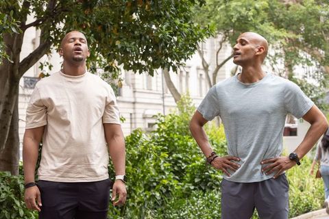 Two african american men cooling down and chatting in urban park wearing smartwatches