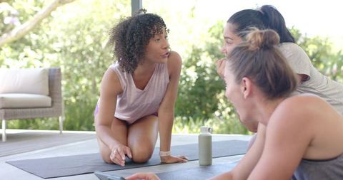 Multiethnic women practicing yoga on sunny outdoor deck leading group workout session