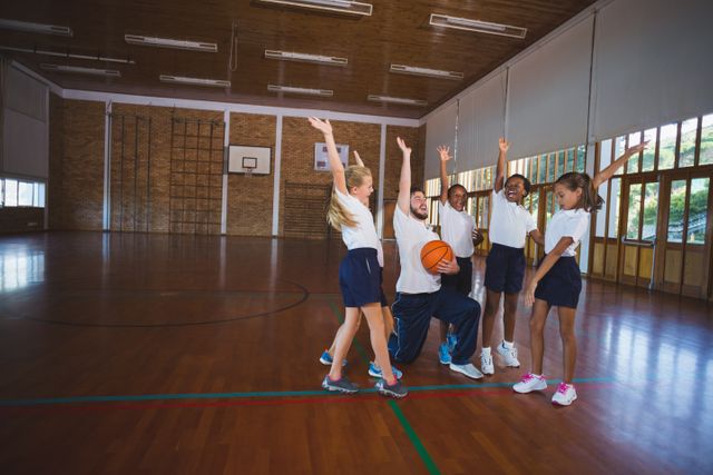 Excited sports teacher and school kids playing in basketball court at school gym