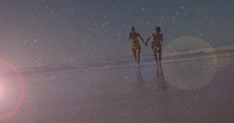 Couple running hand in hand on wet sand at sunset with lens flare and reflections