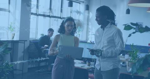 Coworkers Collaborating Over Laptop in Modern Office with Natural Light and Plants