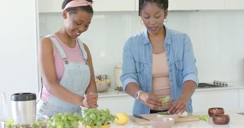 African american mother and daughter cooking together at bright modern kitchen island