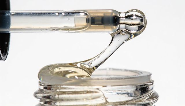 Macro glass dropper dripping viscous skincare serum with suspended bubbles and glints