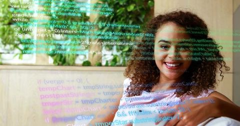 Smiling woman coding with colorful code overlay on modern lounge couch