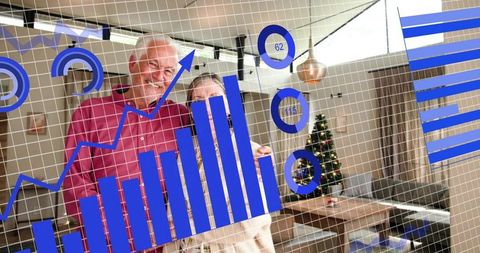 Smiling senior couple reviewing digital financial charts in cozy home with Christmas tree