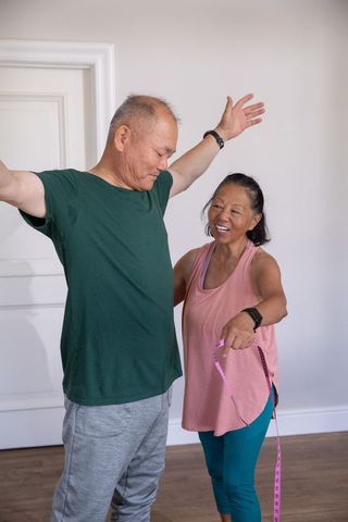Senior asian couple measuring waist with tape while wearing smartwatches for active wellbeing
