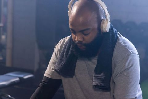 African man resting after workout wearing headphones and towel on shoulders, gym close-up
