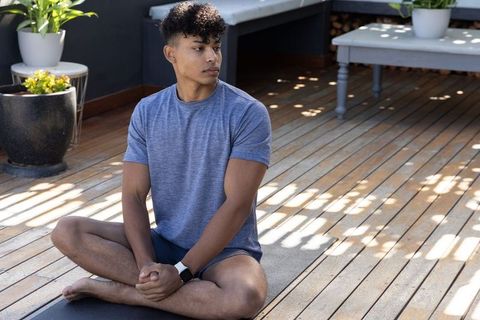 African american man practicing seated meditation on sunlit wooden terrace with smartwatch