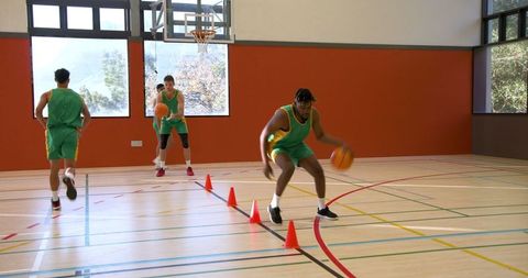 Male basketball players dribbling through cone drills in gym