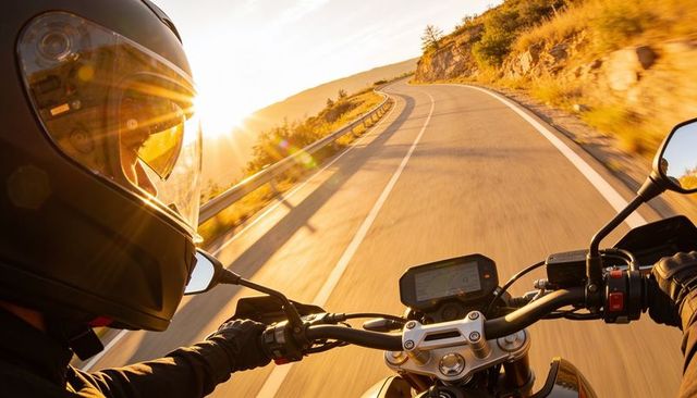 Sunlit motorcyclist riding winding mountain road at golden hour pov action