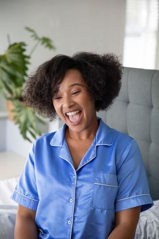 Joyful woman laughing in comfortable silk pajamas in bedroom