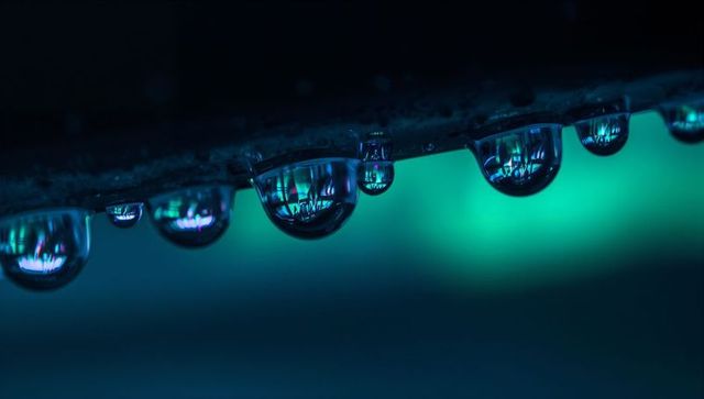 Hanging water droplets reflecting neon lights with teal bokeh and inverted reflections