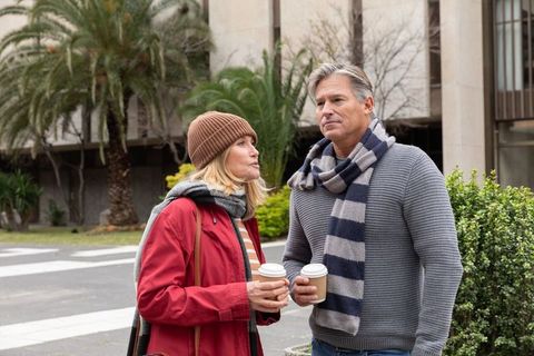 Middle-aged couple holding coffee cups on urban campus plaza wearing scarves and jackets