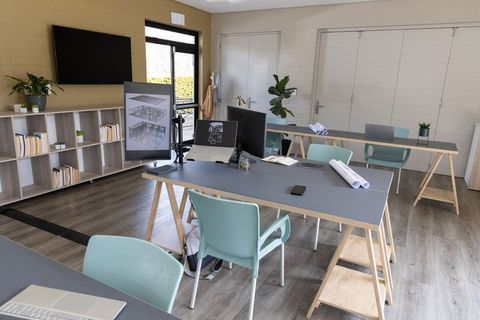 Coworking studio with trestle desks and monitors showing architectural blueprints
