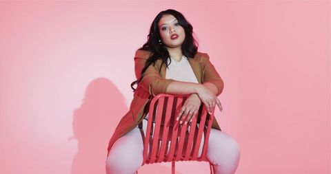 Confident Woman in Tan Blazer on Red Chair in Pink Studio