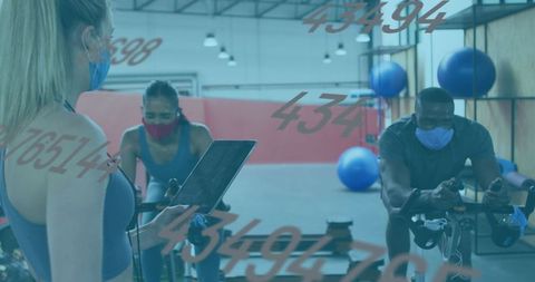 Masked Gym Spinning Class with Instructor Holding Tablet