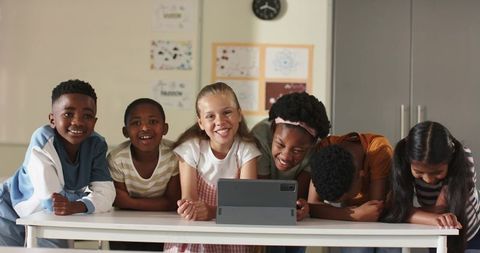 Multiracial Elementary Students Leaning Over Tablet Smiling and Collaborating in Classroom