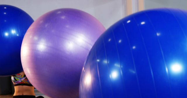 A person is partially visible behind large purple and blue exercise balls, with copy space. Exercise balls are commonly used in fitness routines for core strengthening and balance training.