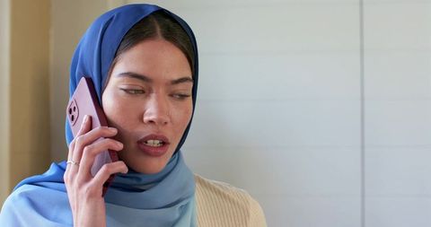 Indian woman wearing blue hijab talking on smartphone minimalist indoor portrait