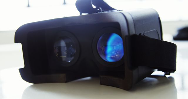 Close-up of a black virtual reality headset with adjustable straps placed on a table. Lenses visible through the front of the device, showcasing reflection and detail. Ideal for use in articles or advertisements about virtual reality, gaming innovations, or modern technology.