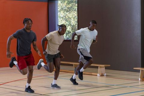 Three men sprinting indoors performing speed and agility training drill in gym
