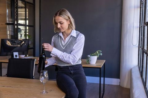 Businesswoman pouring wine in office seeking work-life balance