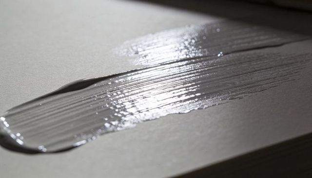 Glossy silver paint brush stroke catching top-left light on textured paper closeup monochrome