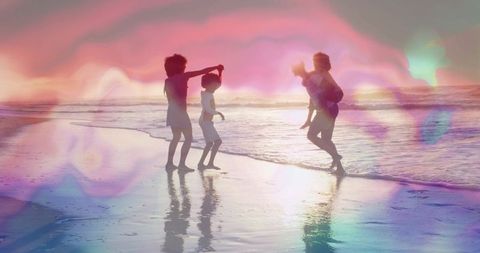 Silhouetted carefree family playing on beach at sunset with pastel lens flare and wet-sand reflectio