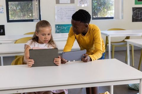 Diverse students collaborating on tablets in modern classroom, teamwork and digital learning