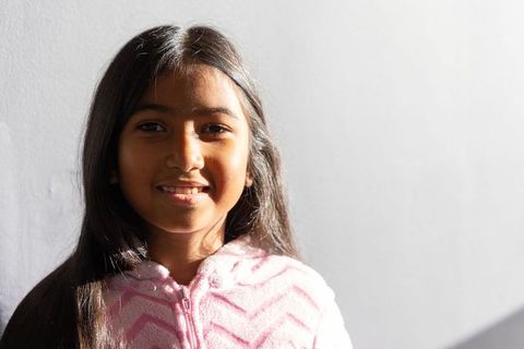 Young girl smiling in warm sunlight wearing pink zip-up fleece with high-contrast shadow