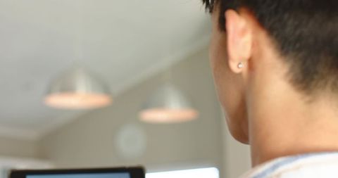 Young man working at laptop showing stud earring in minimalist beige office with pendant lights