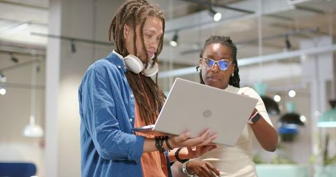 African american coworkers collaborating over laptop in modern open office workspace