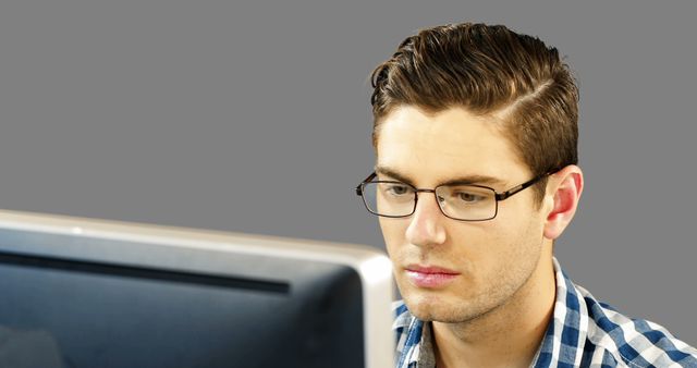 Man with glasses looks focused while working on a computer. Suitable for images related to work from home, technology, professionals, and remote work scenarios.