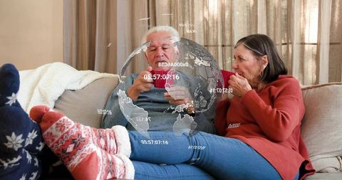 Senior couple sipping coffee on sofa in knit socks and sweaters with holographic globe