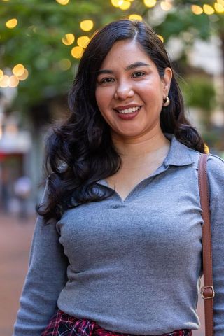 Smiling woman standing in urban plaza at dusk with bokeh lights and casual fall outfit