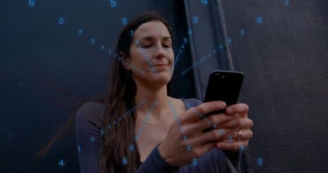 Mid-adult woman using smartphone with numeric data overlay in moody urban alley