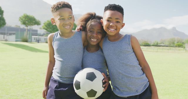 Three young children in casual sportswear are smiling and enjoying playing soccer together on a sunny day in a grassy field. Ideal for themes of childhood, friendship, sports, teamwork, active lifestyle, or summer activities.
