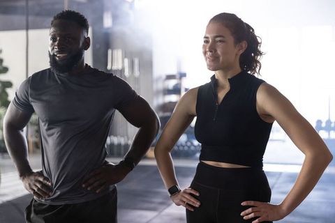 Standing confident workout partners wearing smartwatches in gym, athletic training motivation