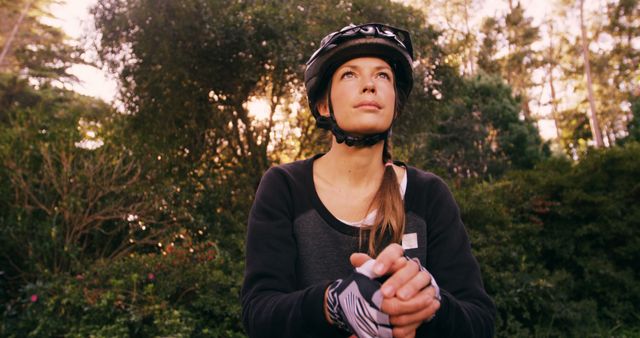 Young woman wearing cycling helmet, enjoying outdoor adventure in natural setting with trees around her. Could be used for promoting outdoor activities, fitness, healthy lifestyle, cycling gear, and eco-friendly travel.