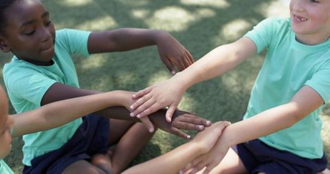 Multiracial schoolchildren placing stacked hands in teamwork huddle on grassy playground
